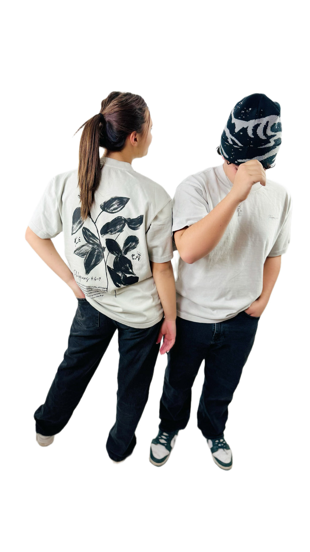 Two people wearing bone  t-shirts with black leaf designs, standing back-to-back on a white background.