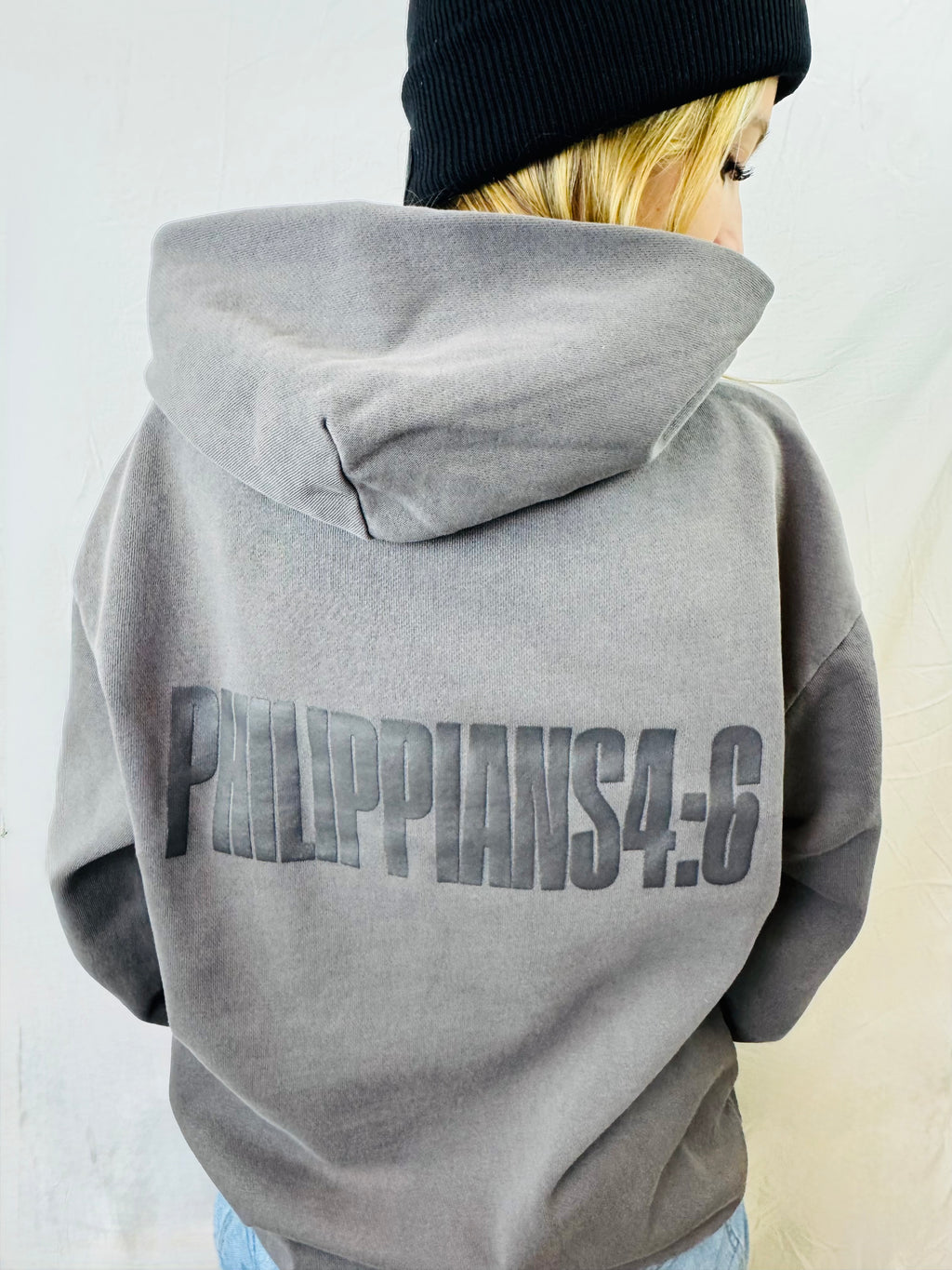 Person wearing a gray hoodie with 'Philippians 4:6' printed on the back, standing against a plain background.