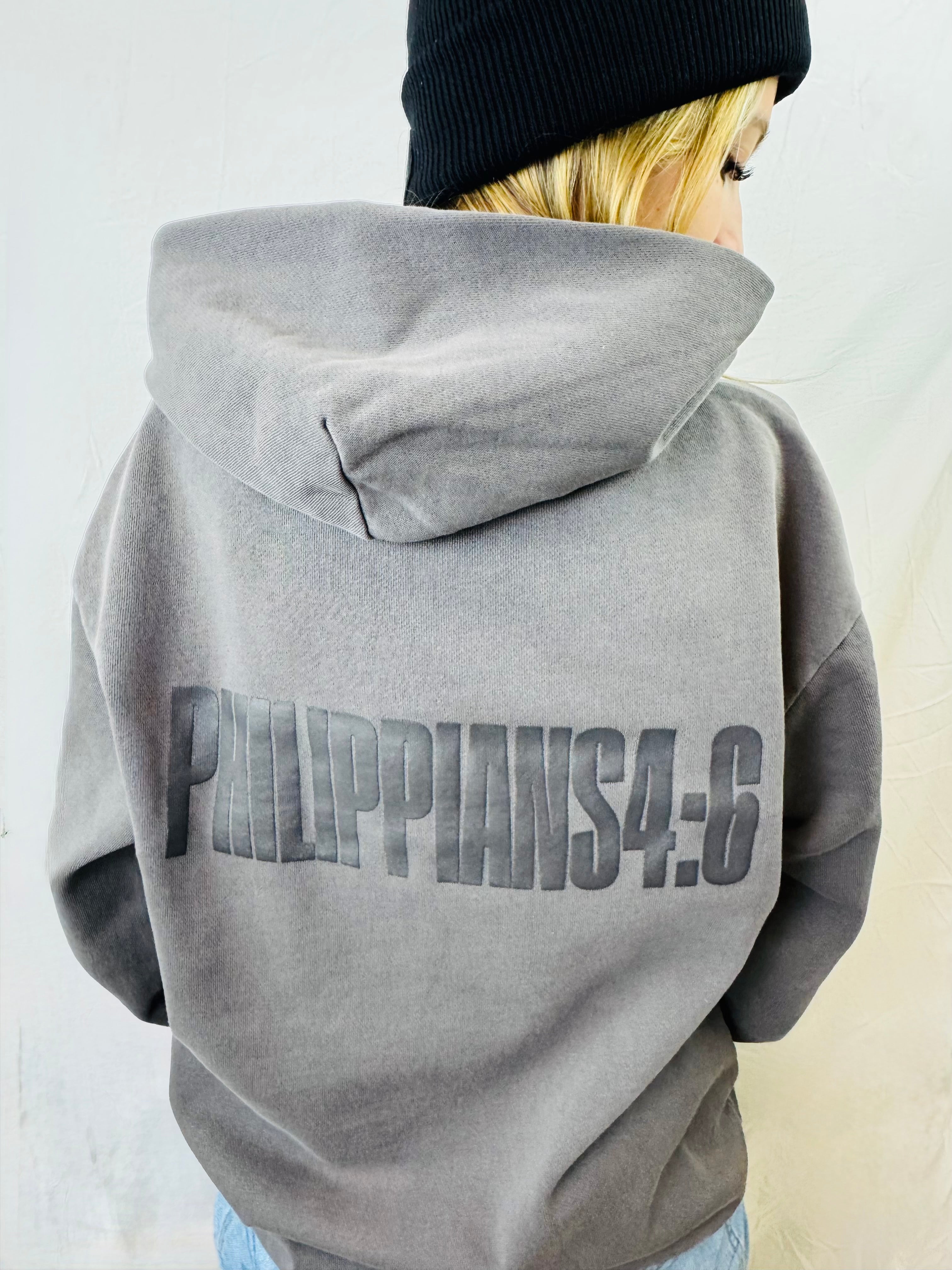 Person wearing a gray hoodie with 'Philippians 4:6' printed on the back, standing against a plain background.