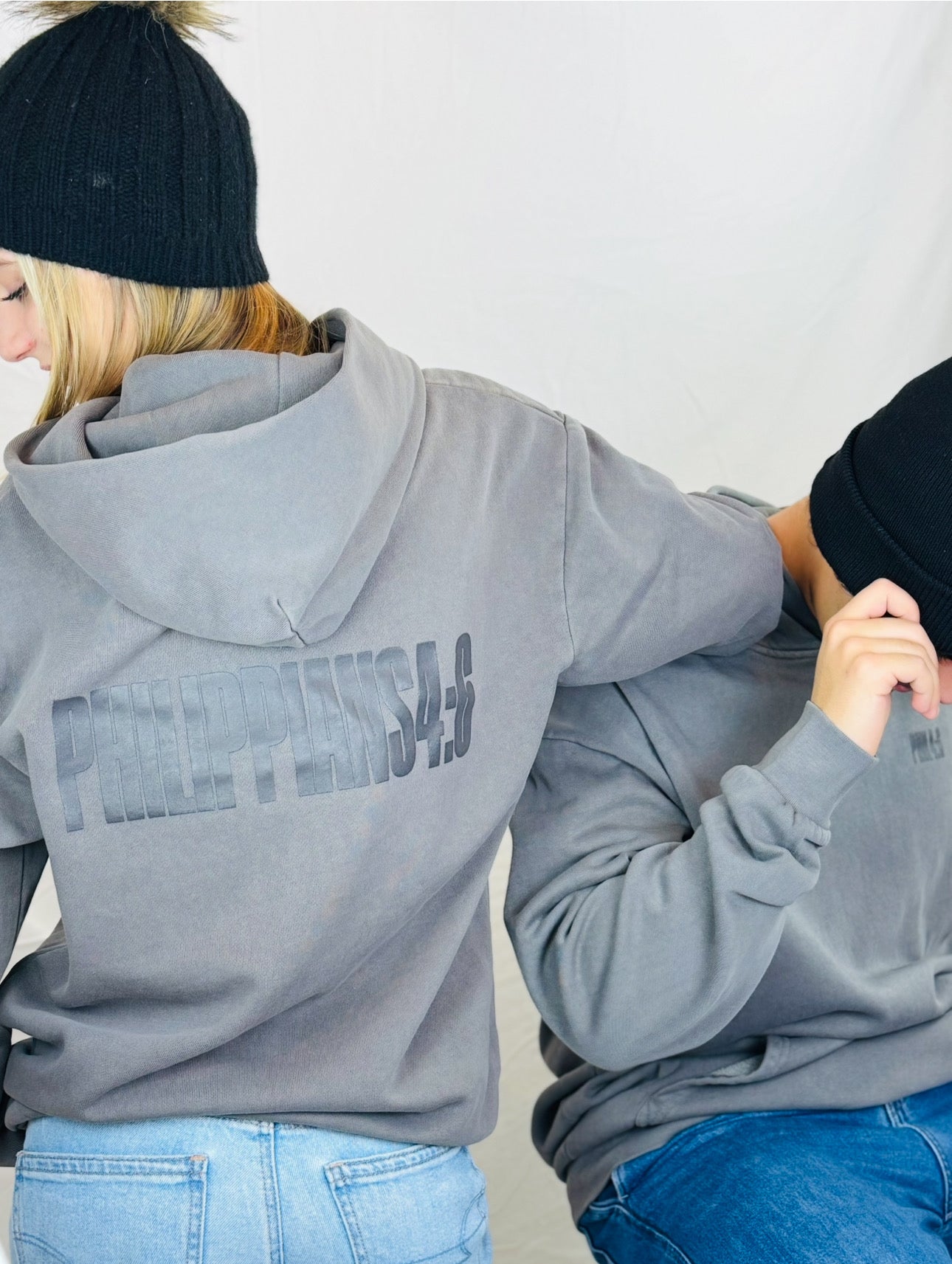 Two people wearing gray hoodies with PHILIPPIANS text, standing close together against a plain background.