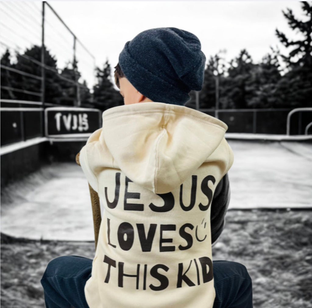 Youth  wearing a cream hoodie with 'Jesus loves this kid' in Chocolate Brown text in an outdoor setting.