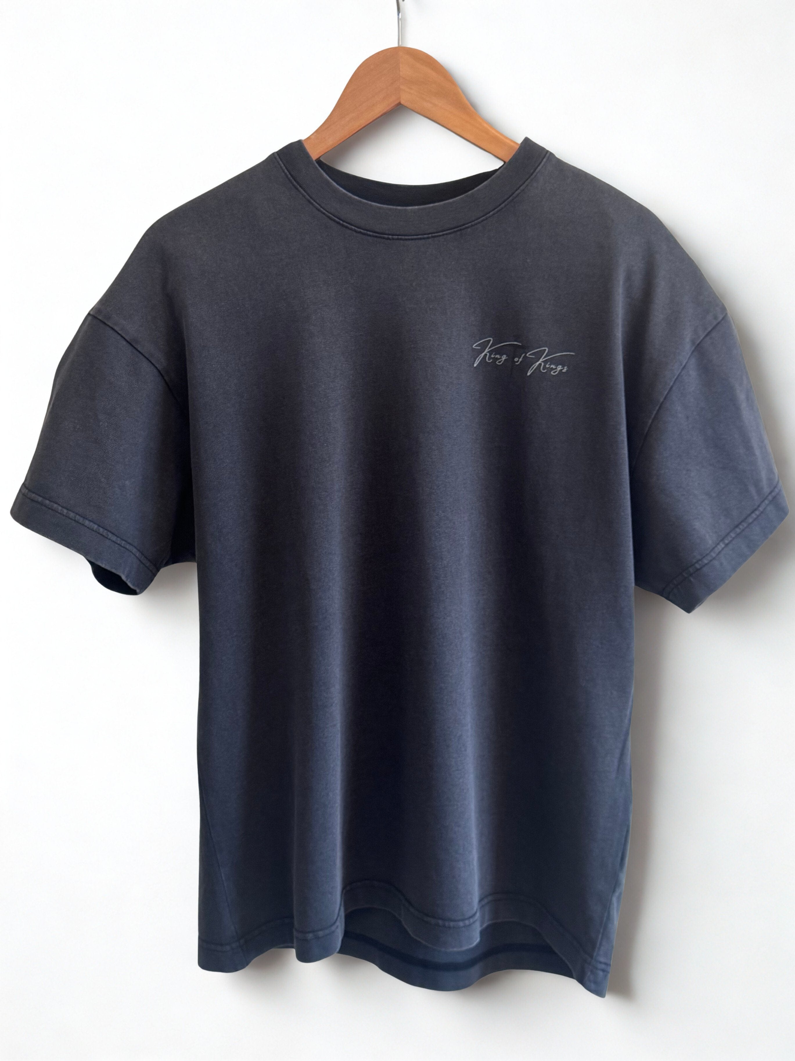 Front of Vintage Black t-shirt with a small black faded cross with small King of Kings overlay on top of cross in light grey lettering on the left chest. 