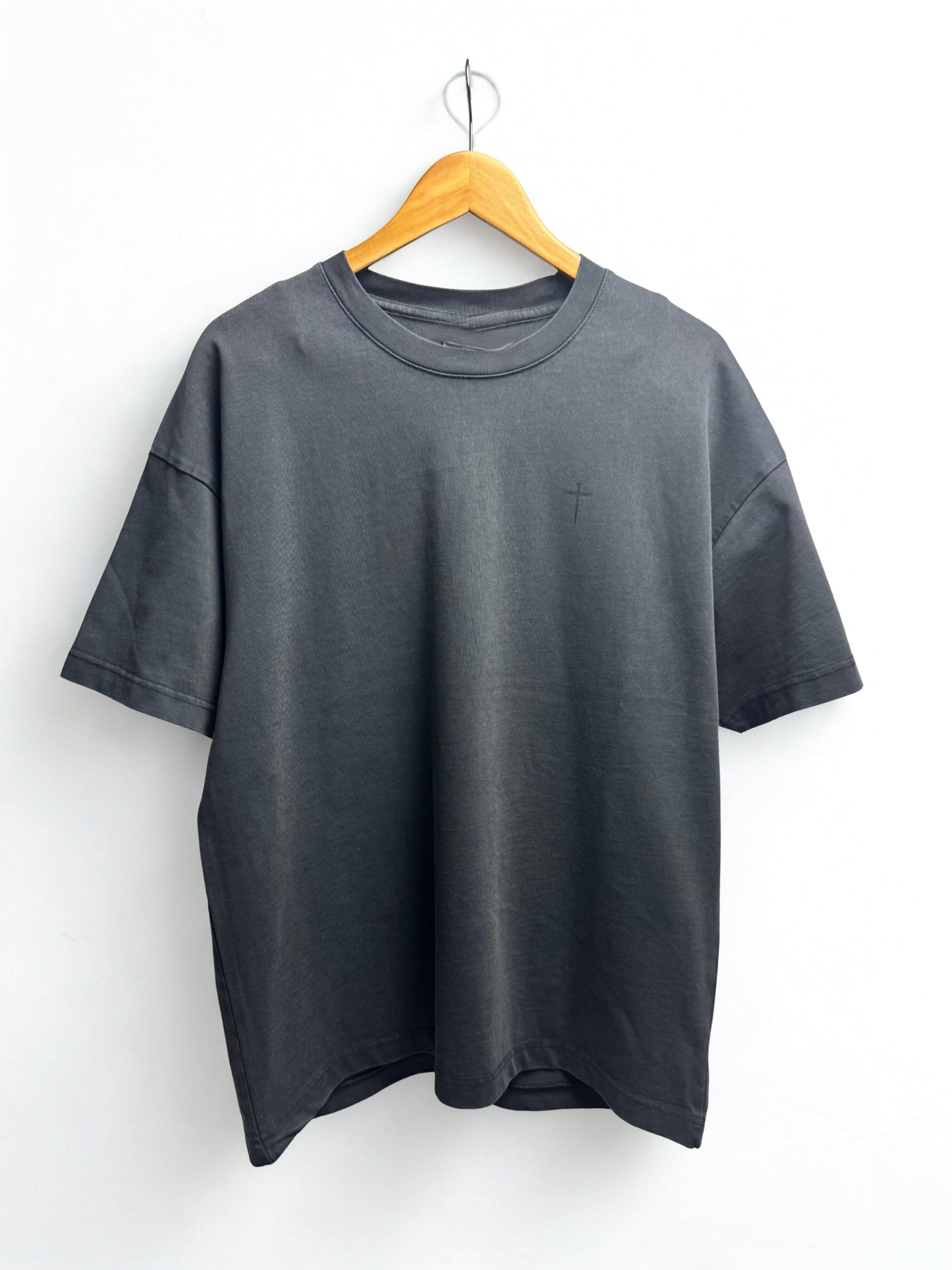 Vintage black  t-shirt with a small black cross on the left on a hanger against a white background