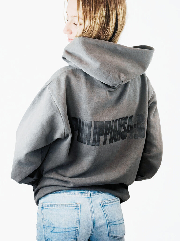 Person wearing a gray hoodie with 'PHILIPPIANS' printed on the back, standing against a white background.