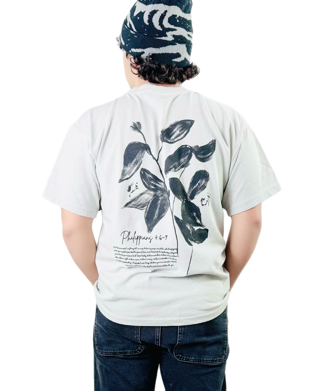 Person wearing a bone t-shirt with a black leaf design and text on the back, standing against a white background.