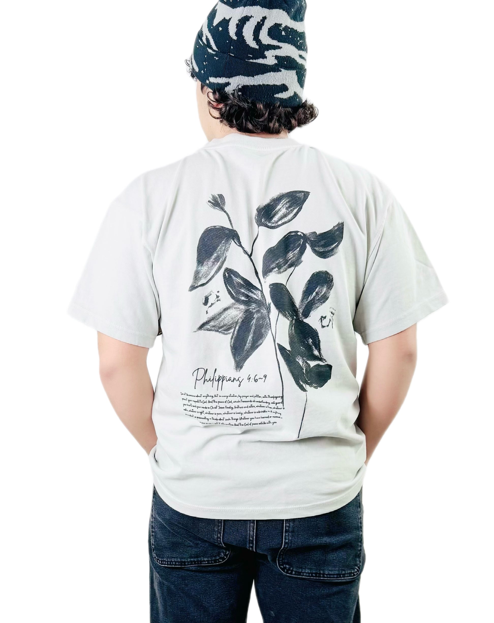 Person wearing a bone t-shirt with a black leaf design and text on the back, standing against a white background.