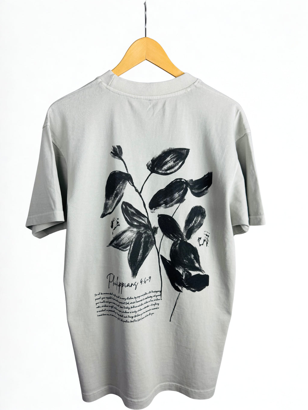 Bone colour t-shirt with black leaf design and black Philippians 4:6-9 scripture on a hanger against a white background