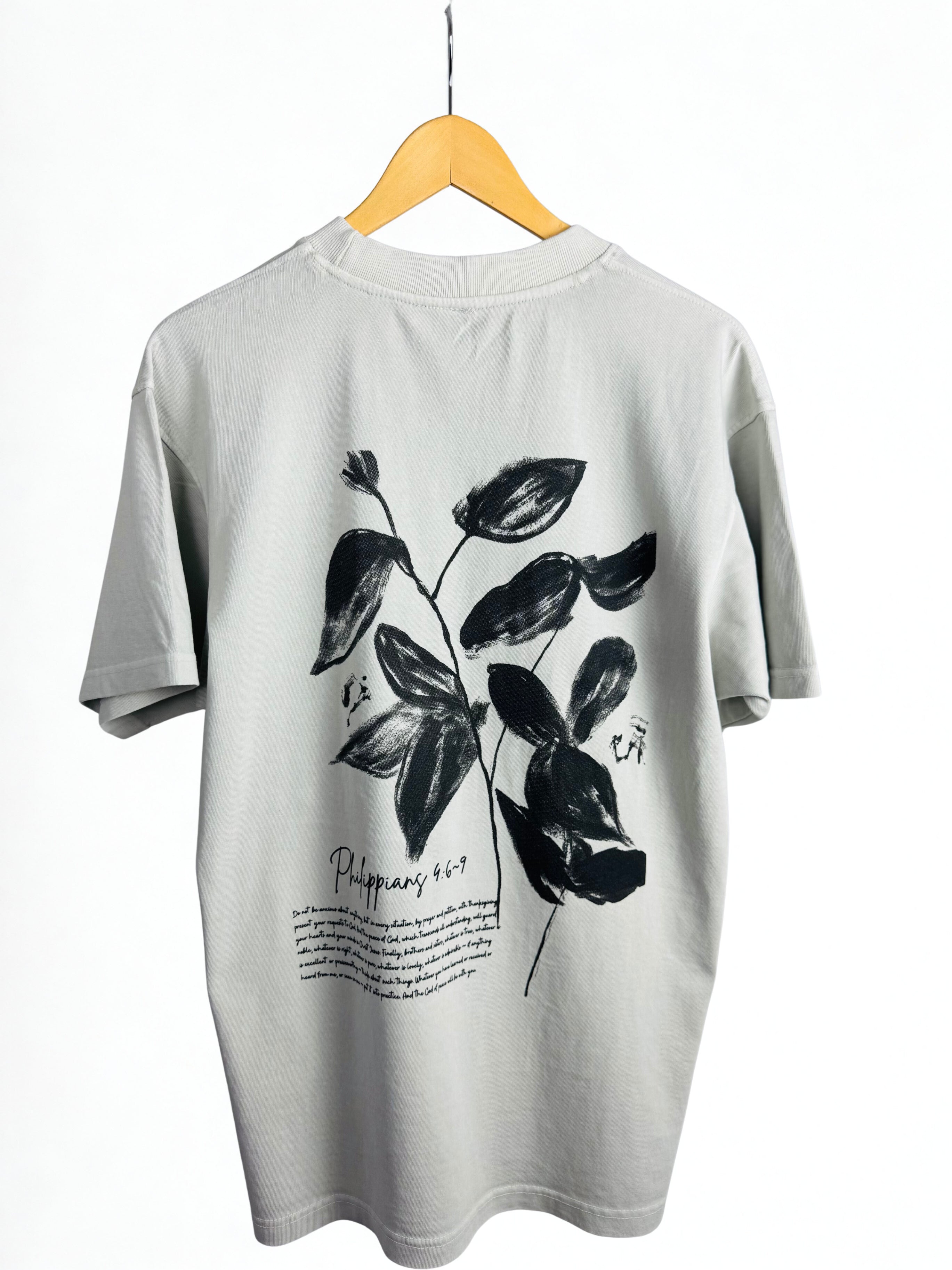 Bone colour t-shirt with black leaf design and black Philippians 4:6-9 scripture on a hanger against a white background